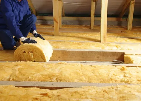 Installer laying fiberglass insulation rolls between ceiling joists
