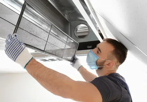 Santa Monica air duct technician in a mask removing a ceiling return filter grille